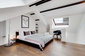 Een moderne slaapkamer met een schuine kap, een groot bed, een bureau en een dakraam.