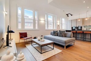 A modern living room with a sofa, coffee table, and a dining area with bar stools. - BR12 - Modern & Stylish 2-Bed Apartment in Borough (Greater London)