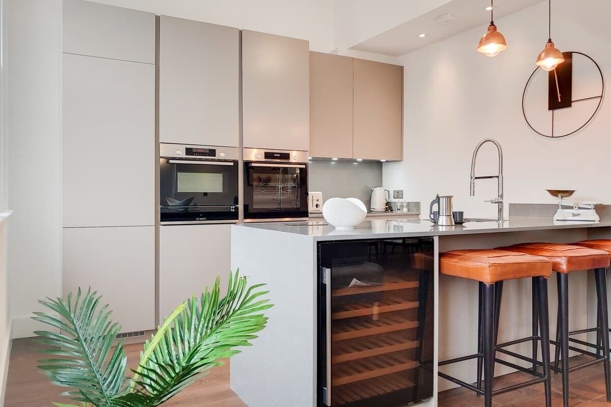 Une cuisine moderne dotée d’appareils électroménagers intégrés, d’un îlot central avec des tabourets et d’un éclairage suspendu.