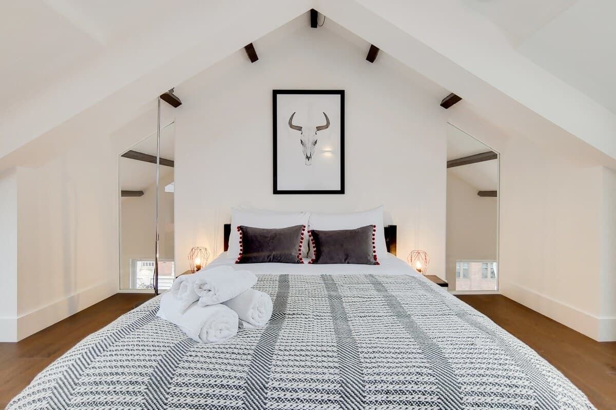 Una camera da letto con soffitto alto, un'opera d'arte raffigurante un teschio incorniciata, una coperta con motivo decorativo e una lampada da comodino.