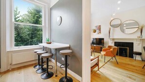 A modern kitchen with a dining area, a large window with a view of trees, and a fireplace. - LG4 - Modern & Spacious 2-Bed in Notting Hill (Greater London)