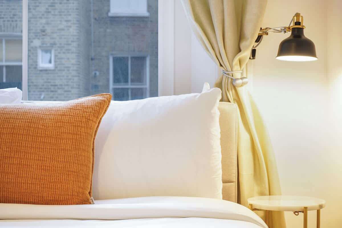 Un lit avec des oreillers blancs et orange, une table de chevet et une lampe.
