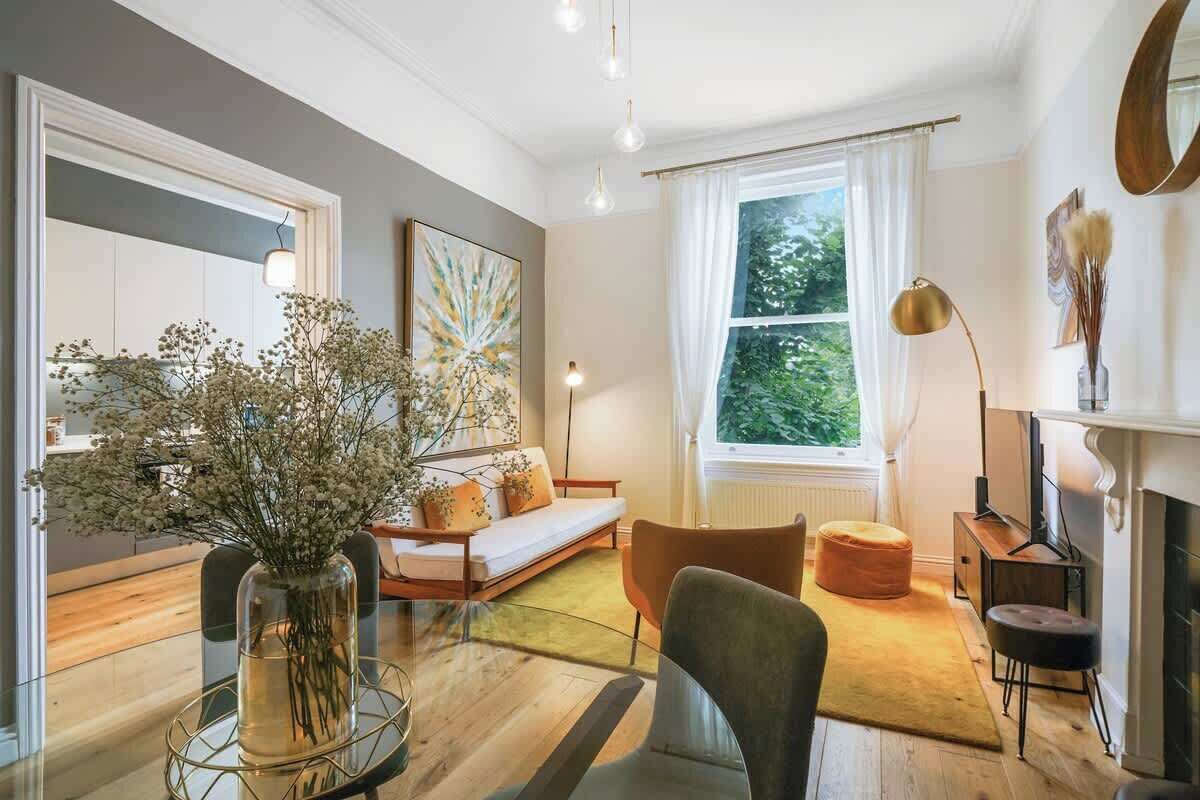 Ein modernes Wohnzimmer mit einer Couch, einem Hocker und einem Glastisch mit Blumen in einer Vase.
