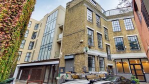 Ein mehrgeschossiges Gebäude mit großen Fenstern, einer Ziegel-Fassade und einer überdachten Außenbereich-Sitzgelegenheit.