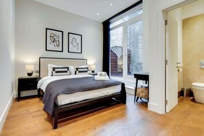 Une chambre moderne avec un grand lit, des tables de chevet, une fenêtre donnant sur un beau paysage et une salle de bain équipée de toilettes et d’un lavabo.