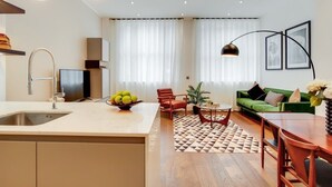 Eine moderne Küche mit Spüle, ein Essbereich mit Tisch und Stühlen, ein grünes Sofa und ein gemustertes Teppich.