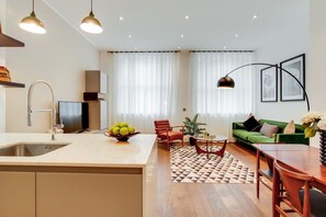 A modern kitchen with a sink, a dining area with a table and chairs, a green sofa, and a patterned rug. - BR8 - Spacious 2-Bed Apartment Near Borough Market (Greater London)