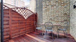 Eine Terrasse mit Holzzaun, Backsteinmauer, Metallstühlen und Tisch.