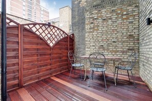 A patio with a wooden fence, a brick wall, and metal chairs and table. - BR8 - Spacious 2-Bed Apartment Near Borough Market (Greater London)