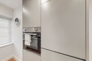 Eine Küche mit Backofen, einer Uhr und einem Fenster mit Jalousien.