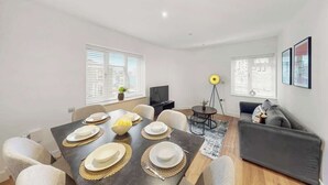 Un salon moderne avec une table à manger pour quatre personnes, un canapé, une lampe sur pied et un téléviseur.