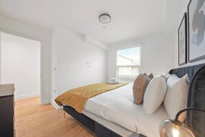 Ein Schlafzimmer mit Bett, Nachttisch, Fenster und Tür.
