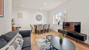 Un salon moderne comprenant un canapé, une table à manger avec des chaises, un téléviseur et une petite table d’appoint.