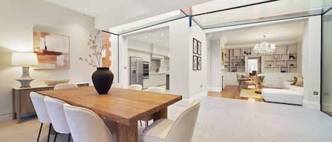 A modern interior with a wooden dining table, white chairs, a vase, and a kitchen in the background.