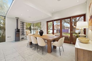 A modern dining area with a large table, chairs, a vase, and a fireplace. - MUR1 - Modern and Stylish 6-bed House in Wimbledon (London)