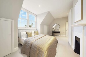 Ein Schlafzimmer mit Bett, Kommode, Spiegel, Kamin und Fenster.