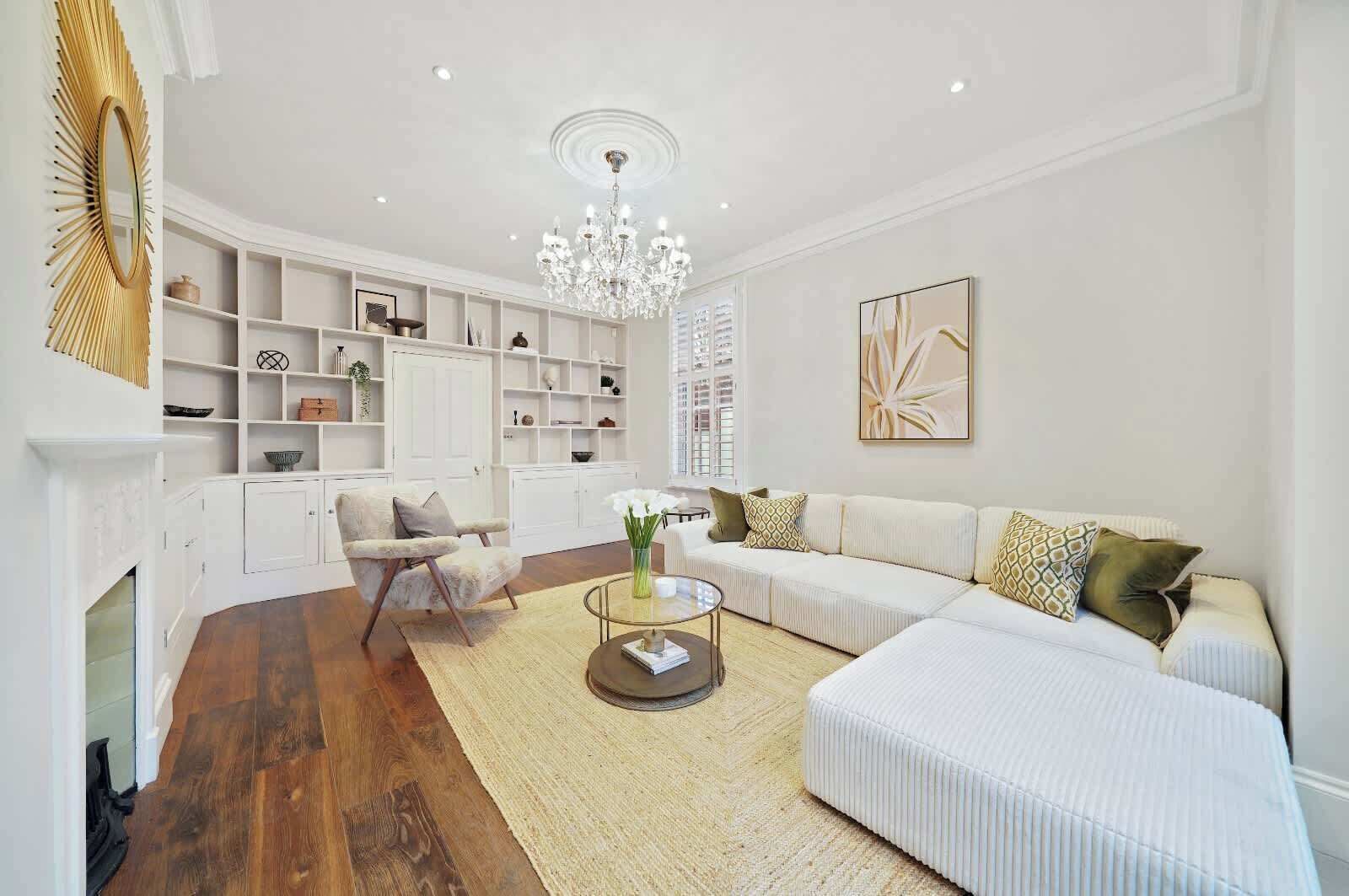 A modern living room with a fireplace, white sofas, a glass coffee table, and a chandelier.