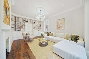 A modern living room with a fireplace, white sofas, a glass coffee table, and a chandelier. - MUR1 - Modern and Stylish 6-bed House in Wimbledon (London)