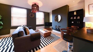 Uma sala de estar moderna com sofá, mesa de centro, televisão e um espaço de jantar com cadeiras.