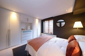 Un dormitorio con cama, armario, espejo, ventana con persianas y una lámpara de pared.