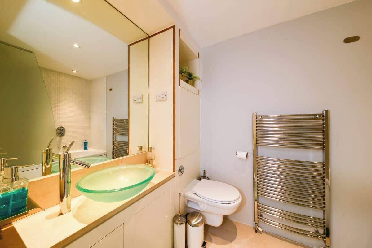 A modern bathroom with a glass sink, a toilet, a towel rack, and a mirror.
