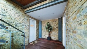 Um corredor com piso de madeira, escada com corrimão metálico e uma porta com o número 2.