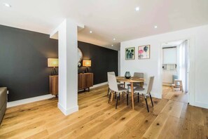A modern living room with a dining area, wooden flooring, and a dark accent wall. - BR7 - Modern 2-Bed Apartment with Private Terrace (Greater London)