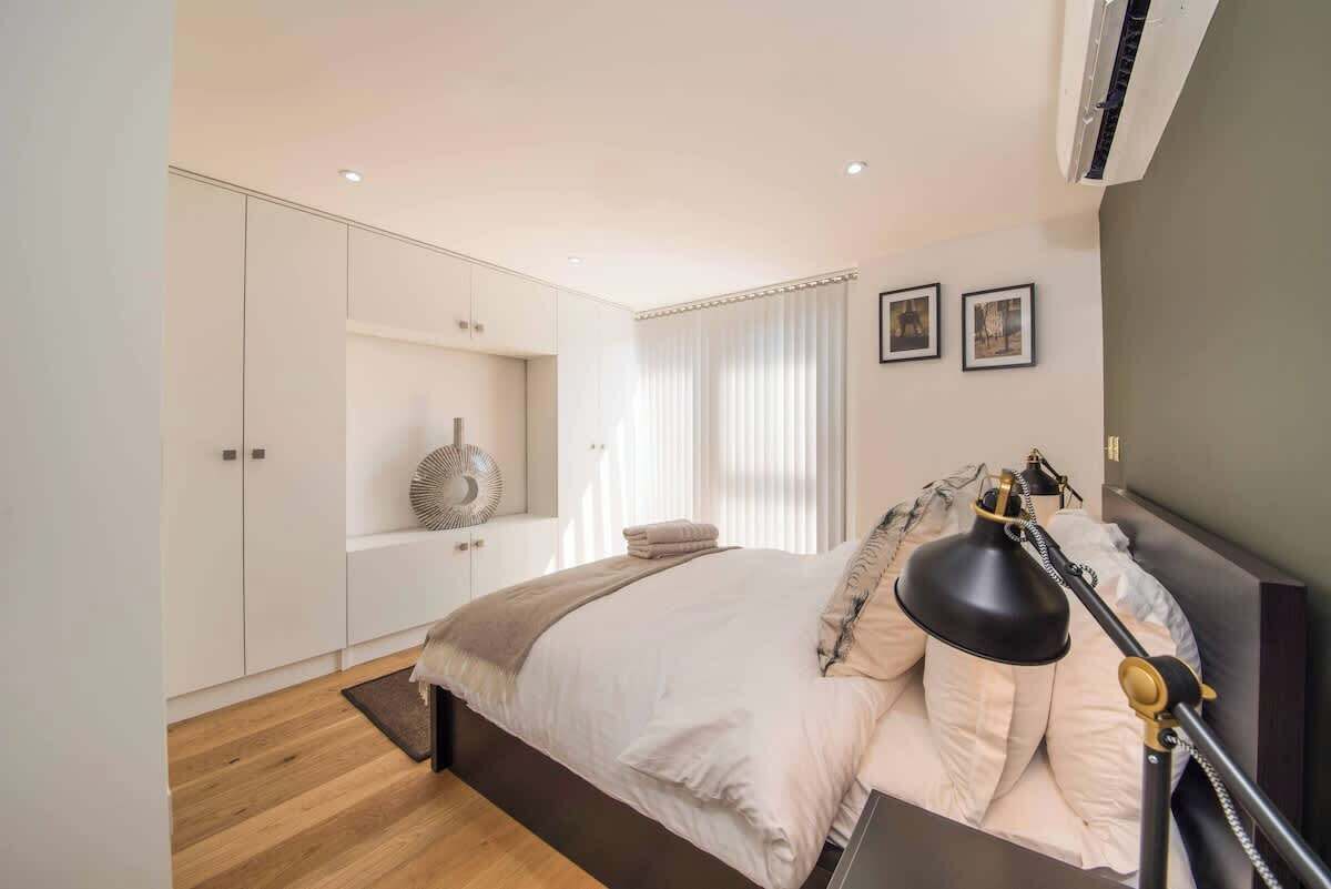 Un dormitorio con cama, lámpara de noche y estante con adornos.
