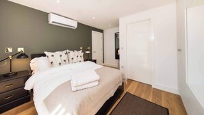 Ein modernes Schlafzimmer mit Bett, Nachttischen, einer Klimaanlage, einem Spiegel und einer Tür.