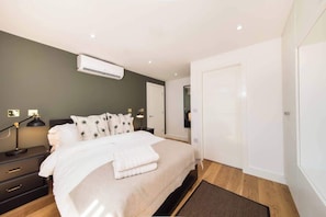 A modern bedroom with a bed, bedside tables, an air conditioner, a mirror, and a door. - BR7 - Modern 2-Bed Apartment with Private Terrace (Greater London)