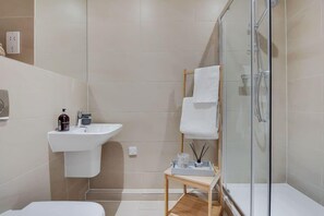 A modern bathroom with a glass shower enclosure, a sink with a soap dispenser, and a small wooden table with a tray. - BR2 - Stunning 1 Bed Apartment Heart of Borough (Greater London)