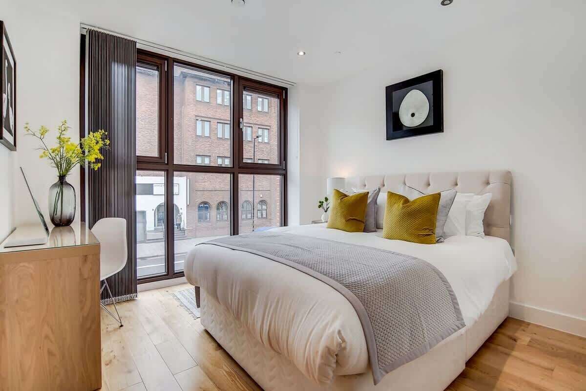 Ein modernes Schlafzimmer mit einem großen Bett, einem Schreibtisch und einem Fenster mit Blick auf Gebäude.