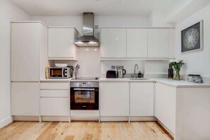 Eine kompakte Küche mit weißen Schränken, einer Mikrowelle, einem Toaster, einem Wasserkocher und einem Backofen.