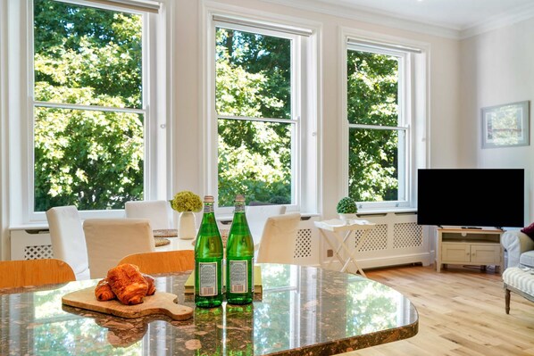 Un coin repas avec une table en verre, deux bouteilles vertes et un croissant.