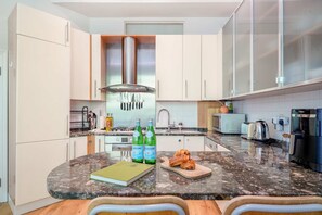 Une cuisine moderne avec des armoires blanches, un comptoir en granit, une cuisinière encastrée et une machine à café.