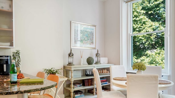 Un coin repas comprenant une table ronde, des chaises, une bibliothèque et une fenêtre donnant sur des arbres.