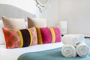 Ein ordentlich gemachtes Bett mit Kissen, einer Nachttischlampe und aufgerollten Handtüchern.