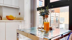 Una cocina moderna con una mesa de vidrio, una planta en maceta y un ventanal con vistas a edificios.