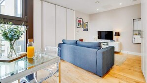 Una sala moderna con una mesa de comedor de vidrio, un sofá azul, un televisor de pantalla plana y un mueble blanco.