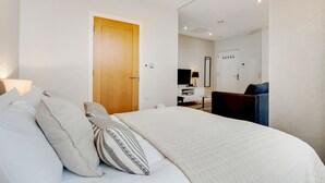Un dormitorio con cama, almohadas, una puerta de madera, un escritorio, una silla y un espejo.