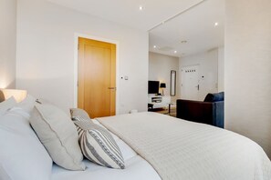 Ein Schlafzimmer mit Bett, Kissen, einer Holztür, einem Schreibtisch, einem Stuhl und einem Spiegel.