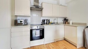 Una cocina moderna con armarios blancos, una campana extractora de acero inoxidable, horno empotrado y cafetera.