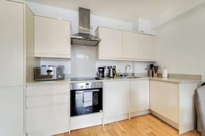 A modern kitchen with white cabinetry, a stainless steel range hood, a built-in oven, and a coffee maker. - BR6 - Beautiful 1 Bed Flat in Heart of Borough (Greater London)