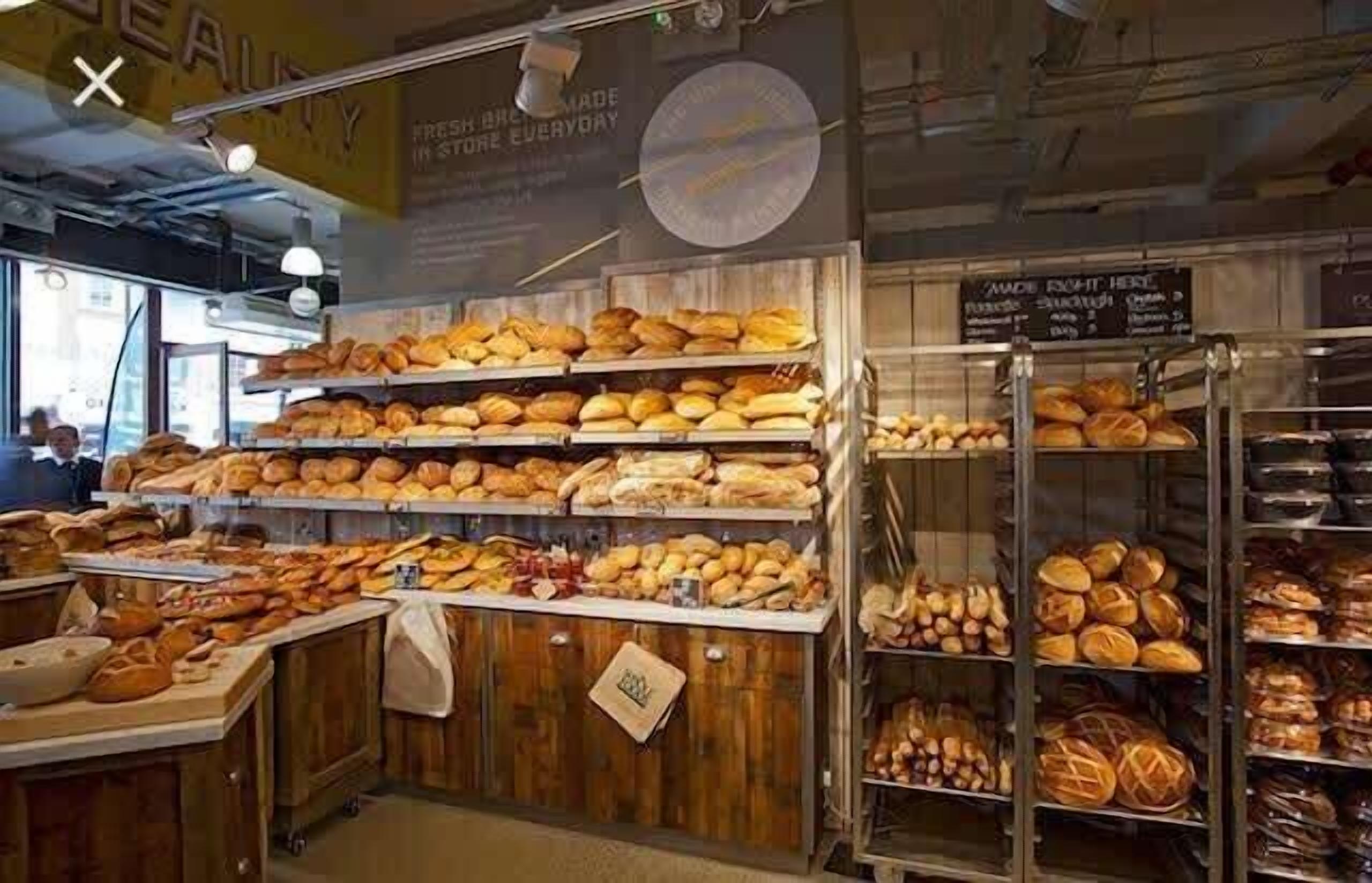 A bakery with shelves of bread and pastries, a sign indicating fresh bread made daily, and a menu board.