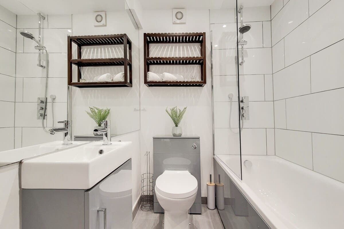Ein modernes Badezimmer mit Toilette, Bidet und Badewanne. Über der Toilette befinden sich zwei Ablagen mit Handtüchern und einer kleinen Pflanze.