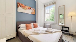 Ein Schlafzimmer mit Bett, einem Bild, einem Fenster, einer Lampe und einem Spiegel.