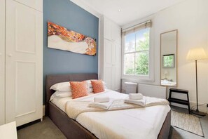 Ein Schlafzimmer mit Bett, einem Bild, einem Fenster, einer Lampe und einem Spiegel.