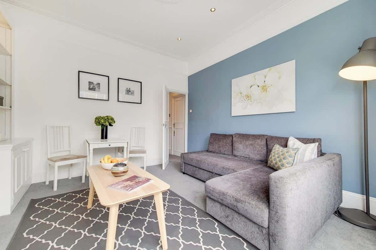 A living room with a grey sofa, a wooden coffee table, a white side table, and a floor lamp.