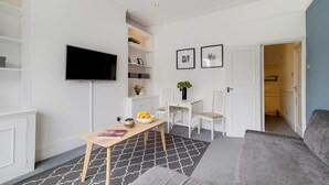 Ein modernes Wohnzimmer mit Flachbildfernseher, Esstisch, einer Couch und einem Flur, der in einen weiteren Raum führt.