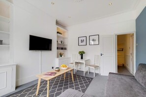 Ein modernes Wohnzimmer mit Flachbildfernseher, Esstisch, einer Couch und einem Flur, der in einen weiteren Raum führt.